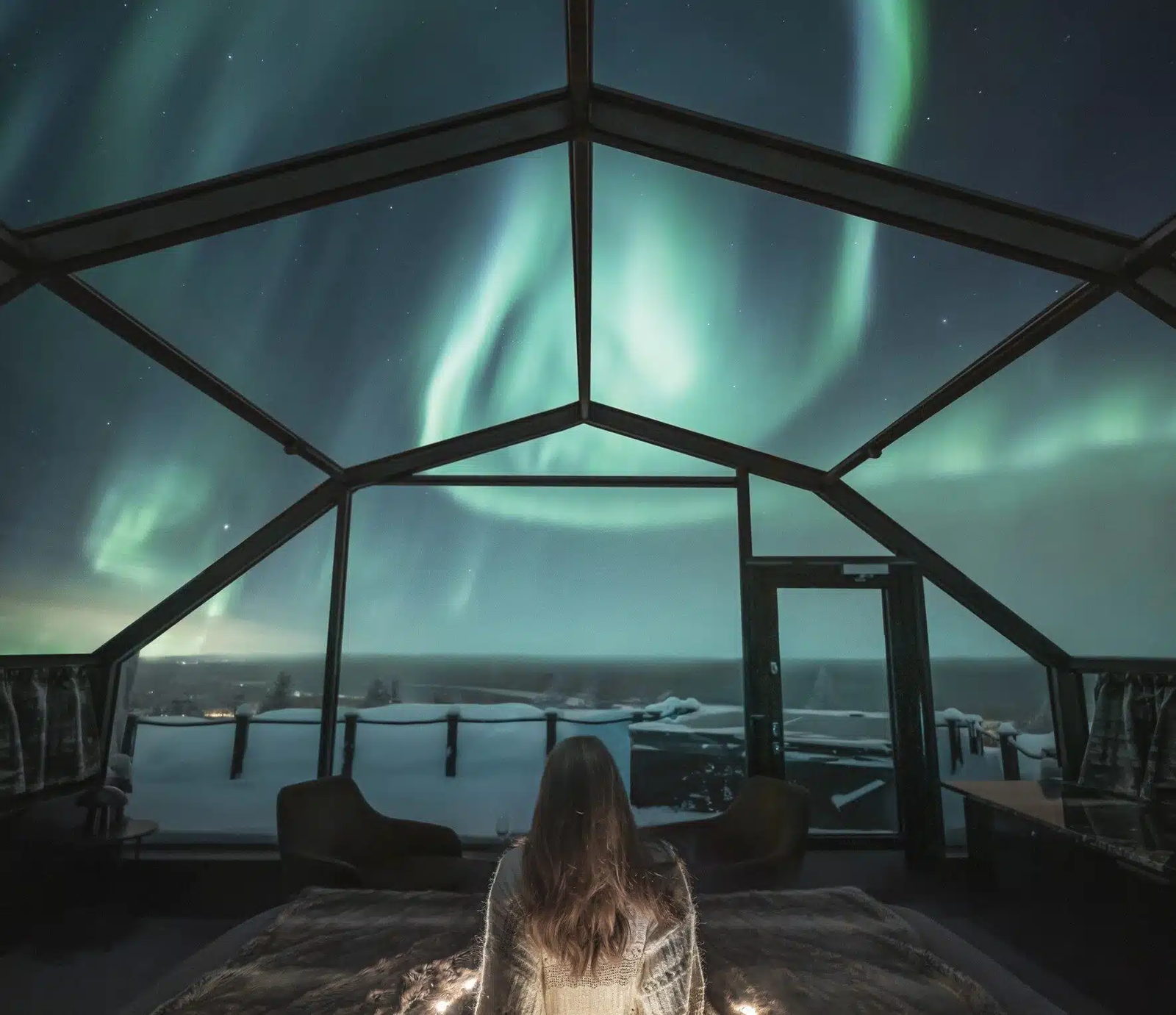 Glass-roofed cabins on a snow slope under a dark northern sky.